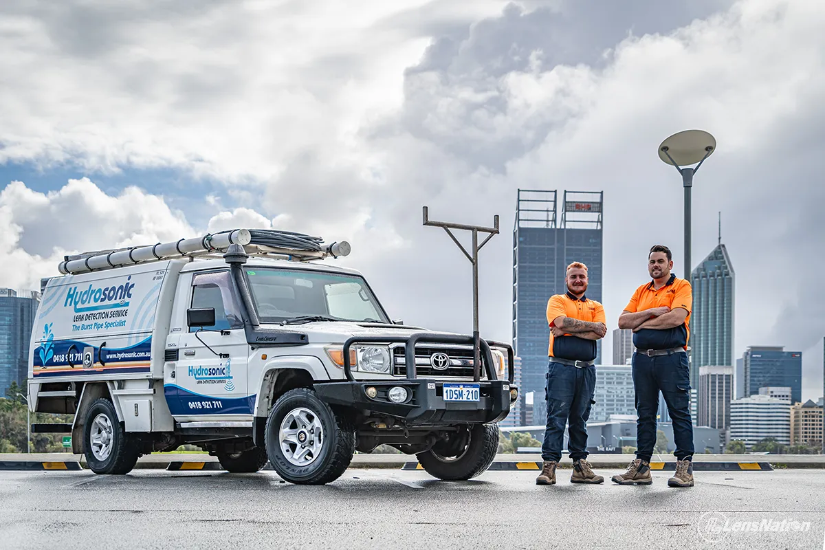 Plumbing business owners standing next to their service vehicle with Perth skyline in background