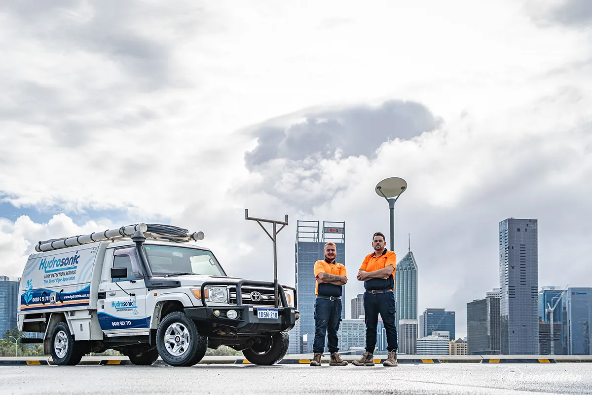 Plumbing team posing with their work vehicle overlooking Perth city skyline